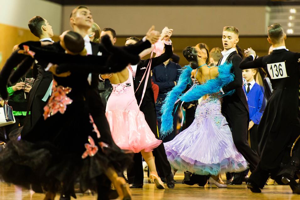 Tanzpaare in eleganten Kostümen tanzen auf einem Parkettboden bei einem Tanzwettbewerb.